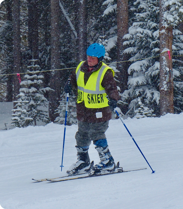 A man heading down the ski slopes wearing a blind skier vest.